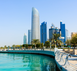 Moderne Skyline von Abu Dhabi mit Hochh&auml;usern an einer Uferpromenade, ges&auml;umt von Palmen und klarem t&uuml;rkisfarbenem Wasser.