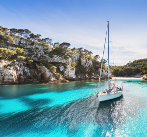 Segelboot in einer t&uuml;rkisfarbenen Bucht zwischen bewaldeten Felsklippen.