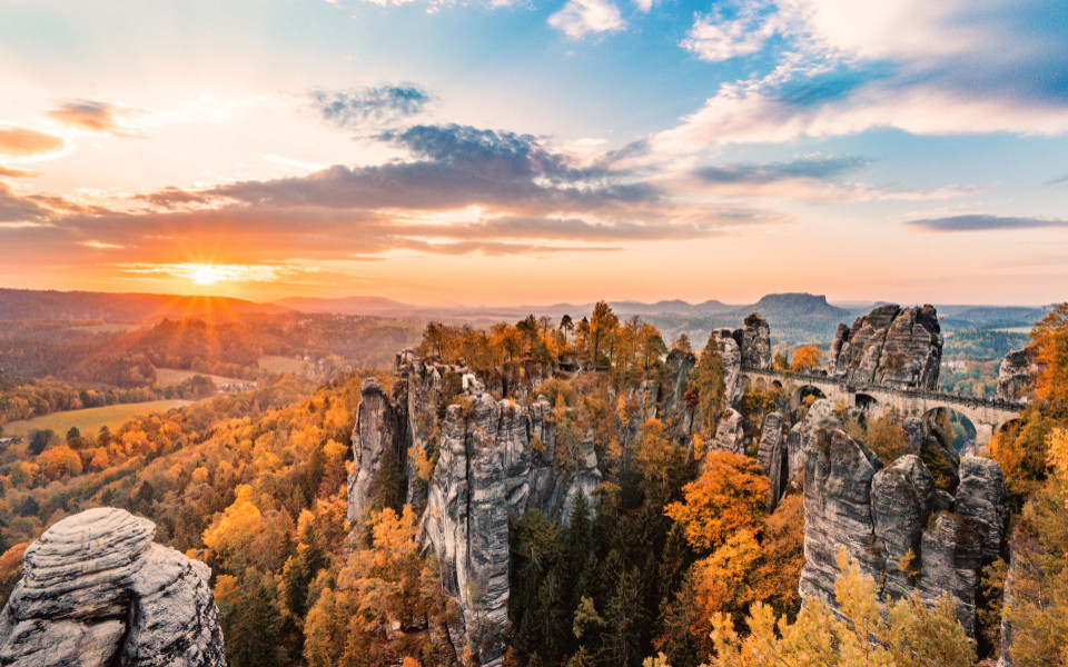 Das Naturparadies Basteibr&uuml;cke im Elbsandsteingebirge, umgeben von beeindruckenden Felsen und mit einem Blick auf die herbstliche Landschaft bei Sonnenuntergang.